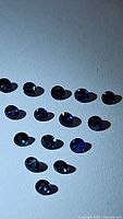 Multiple small round blue sapphires shown arranged in rows on a plain surface, showcasing size, color, and cut.