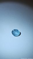 Oval cut natural aquamarine gemstone placed on white background with direct light highlighting its facets and blue color.