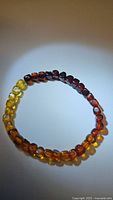 Close-up photo of a stretchy bracelet made of natural Baltic amber beads featuring gradient colors from yellow to dark brown, arranged in a circular shape on a white background.