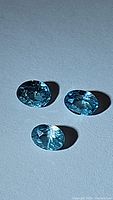 Three oval cut light seafoam blue zircon gemstones on a neutral background displaying facets and clarity.