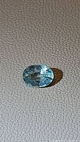 Oval cut natural seafoam blue Cambodian zircon gemstone placed on textured surface, clear and transparent with visible inclusions.
