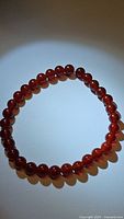 Photo displaying polished round beads of a natural carnelian bracelet with deep red-orange coloration in a circular form.