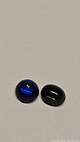 Two cabochon sapphires on a white surface, royal blue on left and teal green on right, viewed from above