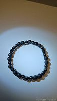 Top-down photo of circular stretchy bracelet made of natural hematite and black onyx beads arranged alternately.