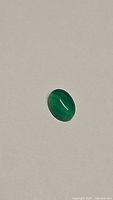 Oval cabochon green onyx gemstone showing vivid green color and smooth polished surface on plain neutral background.