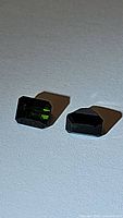 Pair of natural green tourmaline gemstones placed on a white surface, showing their rectangular cut from a front angle.