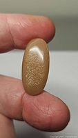Photo showing a close-up of a peach moonstone oval cabochon gemstone held between fingers, displaying sparkly inclusions and smooth polish.