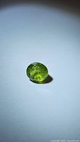 Round-cut apple green natural peridot gemstone placed on a white surface with visible inclusions inside the stone.