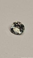 Clear image of a 2.05 carat round cut prasiolite gemstone with pale green coloration on grey background.