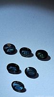 Photo showing six oval natural blue-green sapphires on a light background with visible inclusions and facets.