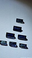 Seven natural blue sapphires laid out on a white fabric background showing variations in cut, color, and visible inclusions.