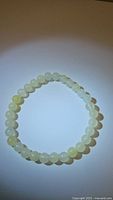 Photo of the white jade beaded bracelet laid flat in a circular shape on a plain background, showing the round polished beads all around the bracelet.