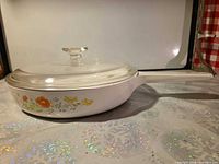 Side view of skillet with lid showing floral pattern, handle, lid knob