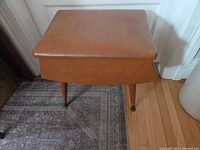 Front view of brown vinyl mid-century storage ottoman on brass-capped legs