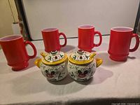Group view of four red mugs and two PY sugar pots with lids and spoons