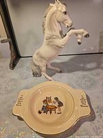 Horse figurine and child’s plate together for scale and composition