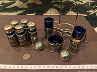 Photo showing four tall antique silver-plated condiment shakers with original cobalt blue glass liners, two shorter containers, two removable silver-plated tops, and metal carrying stand.