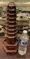 Front angle view of large hand-carved stone pagoda tower next to a water bottle for scale, showing the detailed multi-tiered roof lines and base structure.