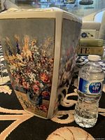 Side view showing large floral artwork on one face of vase next to a water bottle for scale.