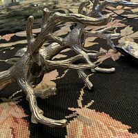 Close-up showing bottom part of a silver metal candle holder with details of tree branch design and central cavity for candle