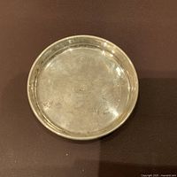 Top view of the small round silver plate showing surface tarnish and engraving on center.