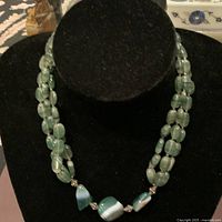 Front view of the necklace displayed on a black necklace stand showing the green polished stones and silver fittings.