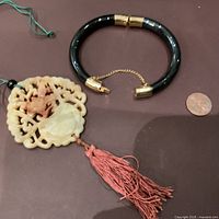 Photo showing both the carved jade pendant with red tassel and the black bangle bracelet next to a penny for scale.