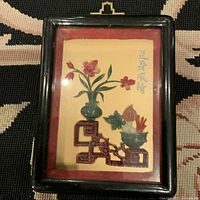 Full view of vintage Asian carved stone art in original black frame showing decorative semi-precious stone floral and fruit arrangement with bilingual script.