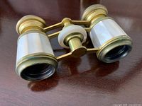 Close-up of the opera glasses showing mother-of-pearl panels and brass frame on wooden surface.