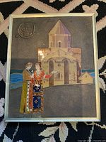 Front view of the framed enamel on metal artwork depicting folklore scene with male and female figures in traditional dress and a building, mounted in original metal frame.