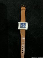Front view of vintage ENDURA wristwatch with rectangular blue dial and tan leather strap on dark background.