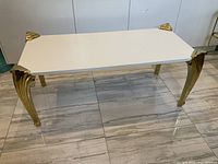 Full view of the rectangular coffee table showing white top and brass legs on a tiled floor.
