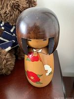 Front view of vintage Japanese Kokeshi doll with floral decoration on body and signed base
