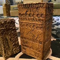 Photo showing two rectangular Mid-Century Modern German brutalist style vases with distinct surface textures and patterns on a black patterned surface with books in the background.