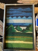 Full view of the framed needlepoint artwork showing the mid-century modern stylized landscape with a metal frame.