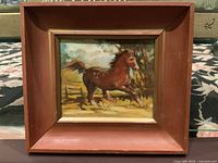 Front view of the vintage oil painting on board of a galloping brown horse with the original frame.