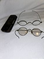 Two pairs of wire frame antique eyeglasses and original leather covered hinged case on white cloth background.