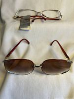 Two pairs of designer glasses frames placed on white fabric, one pair with clear lenses and the other sunglasses with brown lenses