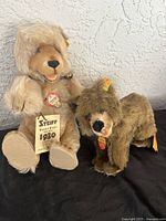 Photo showing both Steiff plush bears side by side on a black surface against a textured white wall.