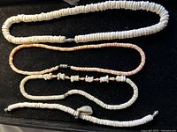 Four items on black background: three puka shell necklaces and one anklet, showing full length and clasp.