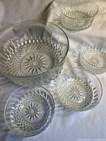 Photo of the complete set including one large bowl and four smaller bowls, arranged on light fabric showing detailed patterns.