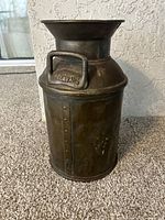 Front side of antique metal Delaval milk jug showing embossed Delaval logo on handle and rivet details.