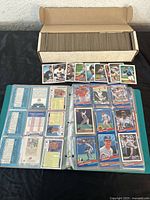 Photo showing a long box filled with 1989 Topps baseball cards and a row of cards laid out in front of the box. Also shows a 3-ring binder with seven pages of baseball cards in protective sleeves.