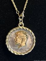 Close-up of pendant showing front face of 1964 Kennedy half dollar coin within decorative gold-tone rope bezel.