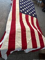 Full length view of the large American flag laid out on floor showing red and white stripes and blue canton area with white stars.