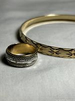 Close-up photo of the gold-tone bangle bracelet with starburst pattern and the silver tone ring with detailed etched and faceted design showing both items together.