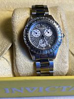 Silver-tone Invicta watch on yellow cushion inside an Invicta box, showing the sparkly dial and bezel