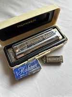Marine Band harmonica in open white plastic case, miniature Tiny harmonica, and original blue box for Tiny harmonica visible