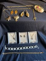 Full assortment of jewelry items arranged on black fabric showing loose necklaces, boxed necklaces, bracelets, earrings, vintage pin, pendants, and ring
