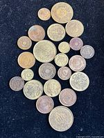 Top view of 23 assorted coins on black background showing various denominations and designs.